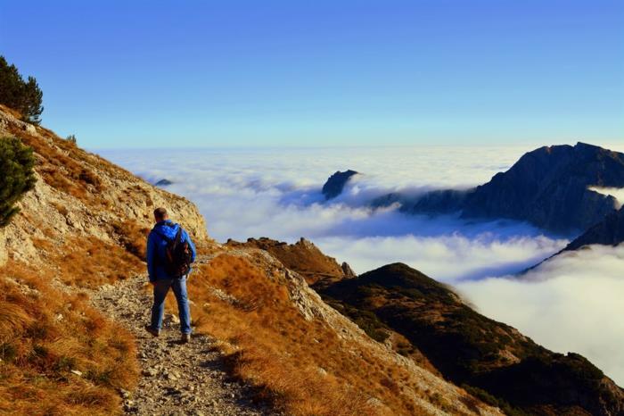 bergigt landskap, man går på en liten sicksackväg i berget, turist som har överträffat molnivån