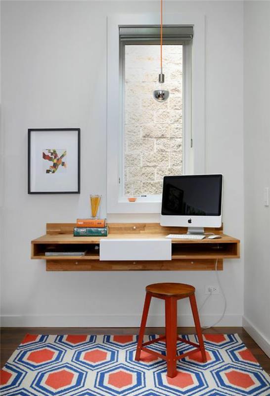 studentrumsinredning, matta med bikupemönster i orange, vitt och blått, hängande skrivbord i ljust trä, storbildsdator, rektangulärt fönster, träpall målad röd, bord i ljusa färger med en tunn svart ram