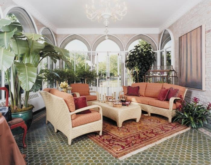 landskapsarkitektur-veranda-i-hörn-av-deco-vila-sammansatt-av-många-exotiska växter-rotting-soffa-orange-säten-brun-soffbord-exotisk-matta-överdådig-ljuskrona