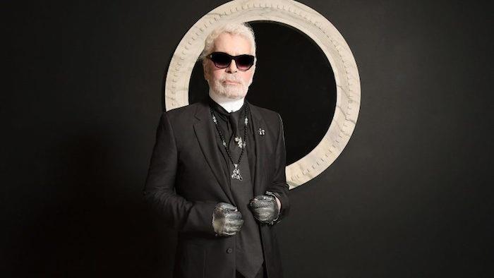fotografia návrhára Chanel Karla Lagerfelda v jeho čiernom obleku s chvostom a čiernymi okuliarmi na čiernom pozadí