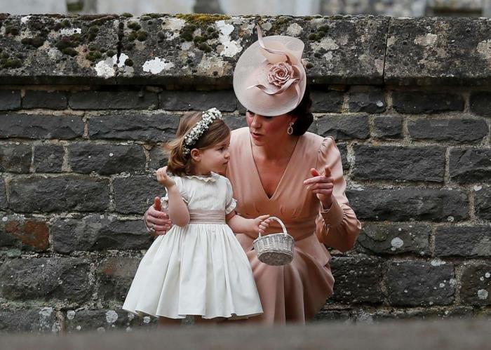 كيت ميدلتون ترتدي فستانًا ورديًا بلون الخوخي وقبعة زفاف نسائية والأميرة الصغيرة بفستان أبيض