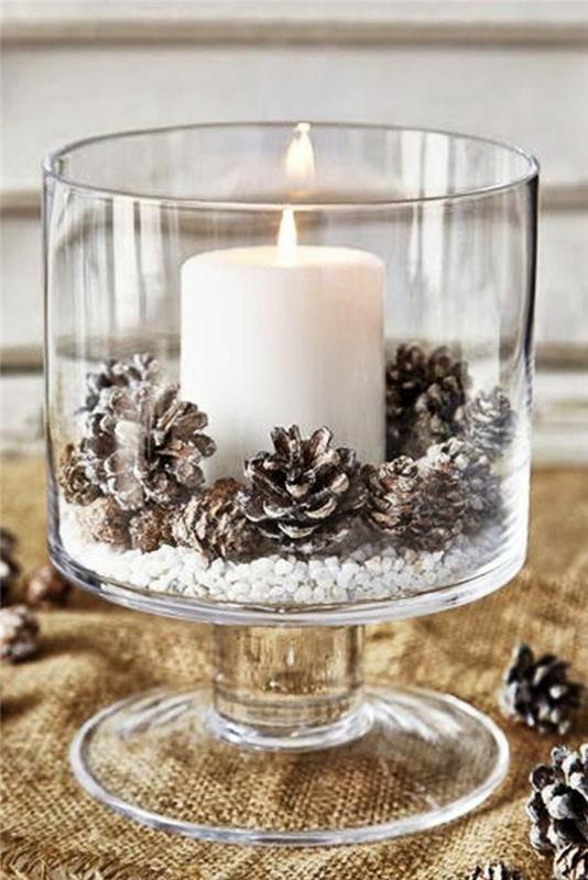 Vianočná dekorácia, aby ste sa ocitli vo veľkej sklenenej miske, s veľkou bielou sviečkou a obyčajnými šiškami, na dne misky malé biele kamienky