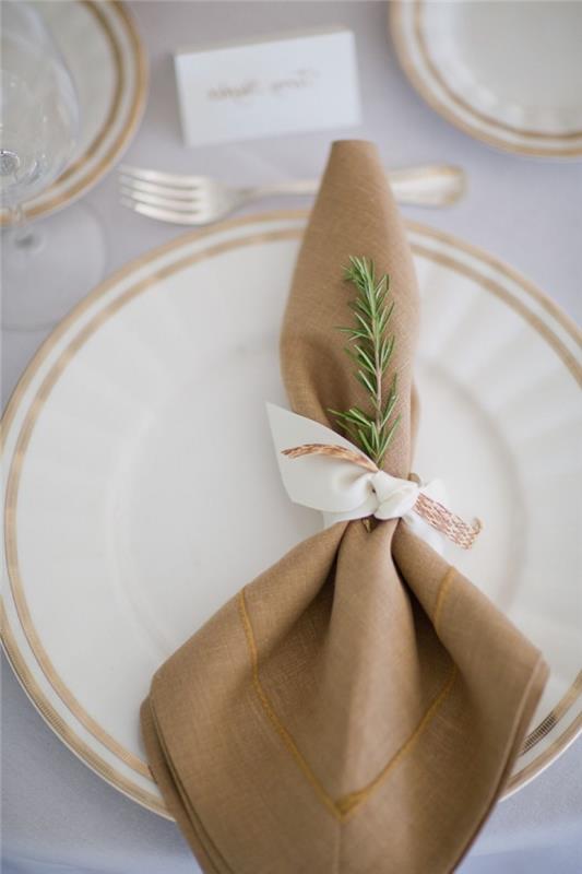 štýlový nápad na dekoráciu stola v bielej a zlatej farbe, príklad jednoduchého skladania obrúskov s bielou stuhou a jedľovou vetvou