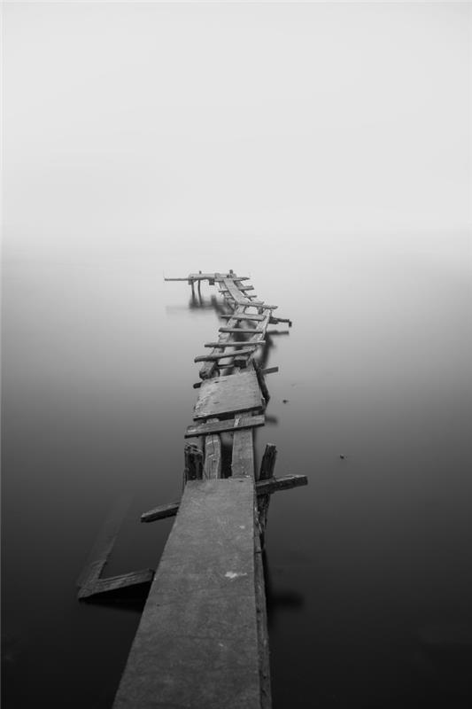 svartvit bild av gammal träbrygga omgiven av lugnt havsvatten