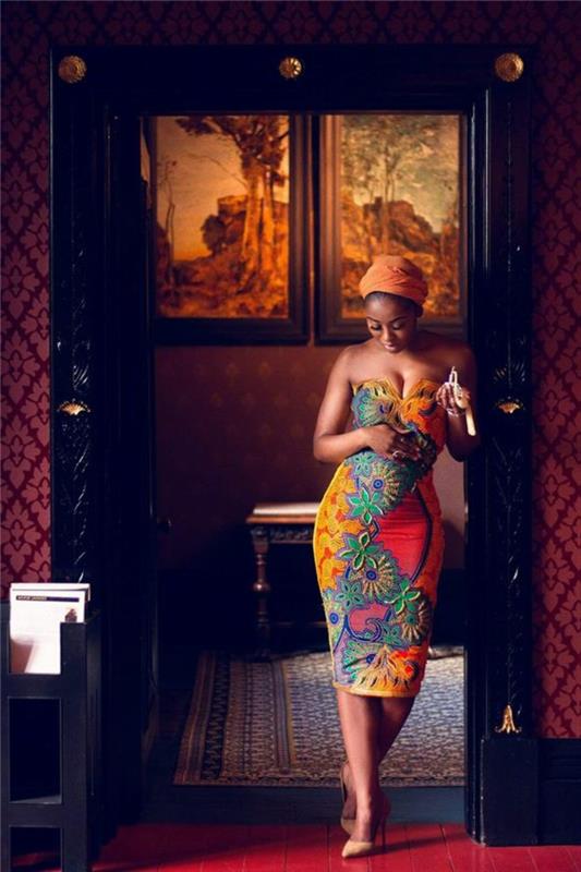 kvinna som står i dörröppningen, klädd i en klänning, afrikanskt tryck, orange huvudduk. nakna klackar