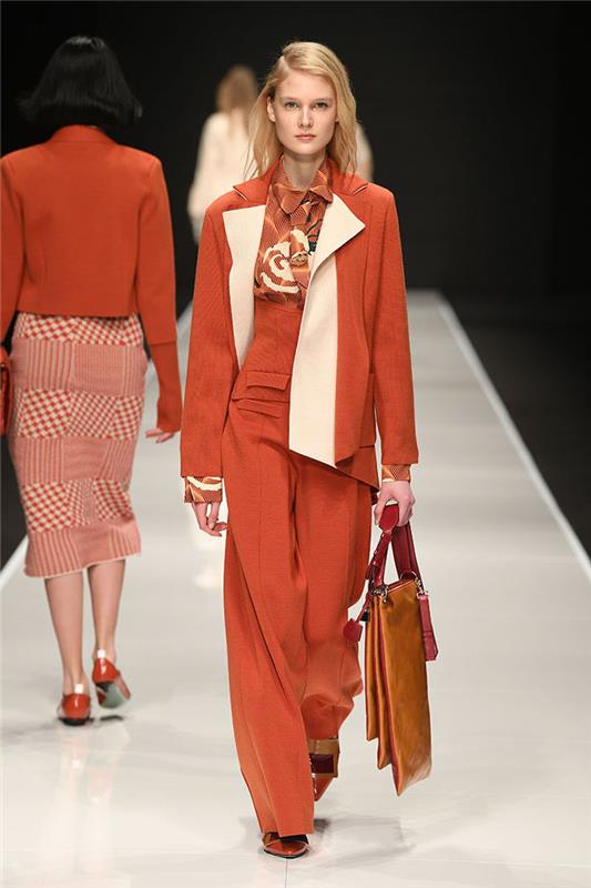 عارضة أزياء تسير على المدرج ، اتجاهات الموضة الحالية ، ترتدي بدلة برتقالية اللون ، تتكون من بلوزة وبنطلون