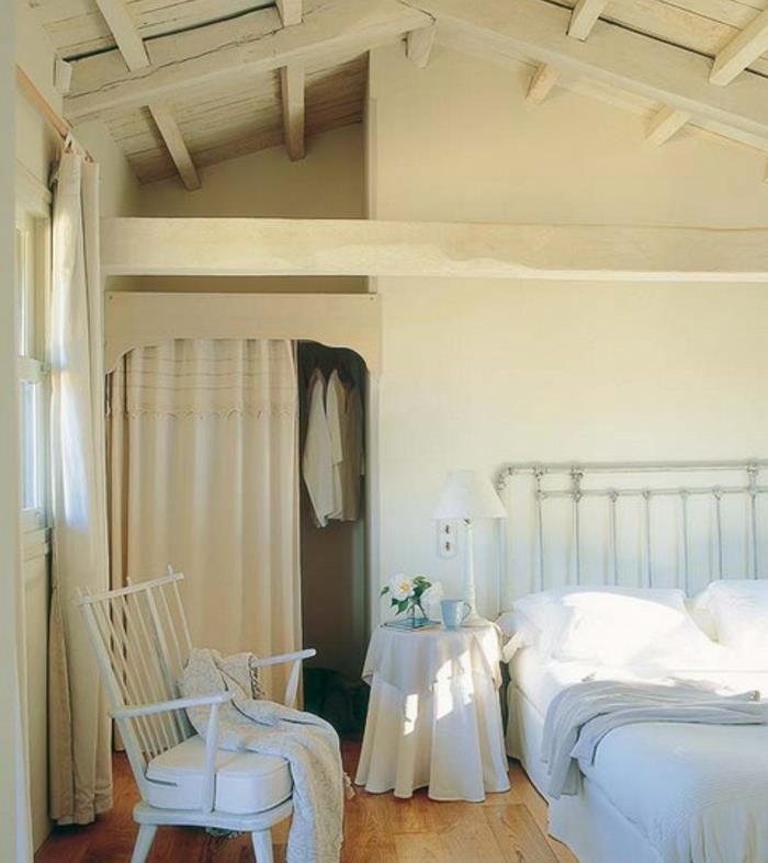 Deco -sovrum under sluttningen, ljus parkett, metallbädd, vita sängkläder, vit stol, takbjälkar i tak, vindsrumsinredning allt i vitt