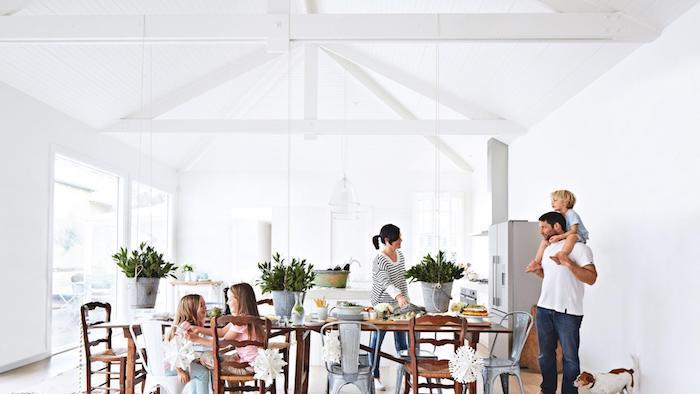 biela dispozícia otvorenej kuchyne vedúca do jedálne s dreveným stolom a stoličkami, zelených rastlín, spotrebičov z nehrdzavejúcej ocele
