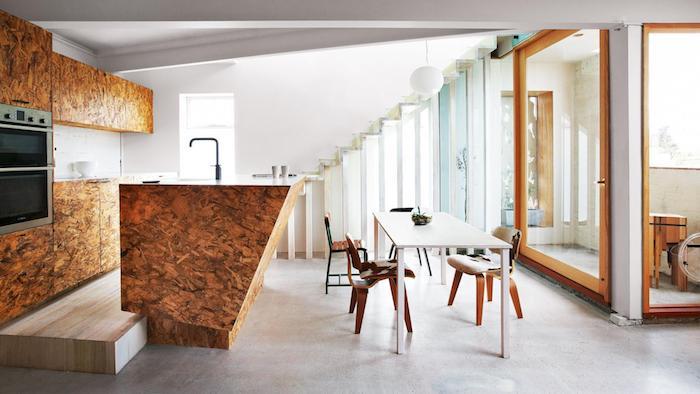 Americká kuchyňa z dreva s centrálnym ostrovčekom z dreva a výstrihom do bieleho obkladu, biely jedálenský stôl a drevené stoličky, veľké okno s výhľadom na terasu