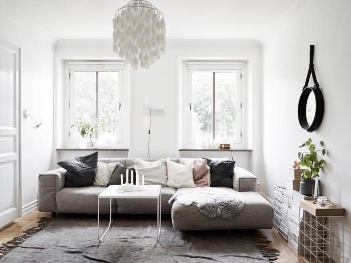 litet monokromt skandinaviskt vardagsrum med en mysig grå soffa täckt med dekorativa linnedynor och en kantad matta