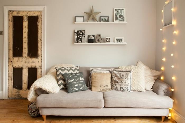 liten relaxavdelning med en mysig beige soffa täckt med kokande dekorativa kuddar av samma ton och en ljus kransdekoration som hänger på väggen