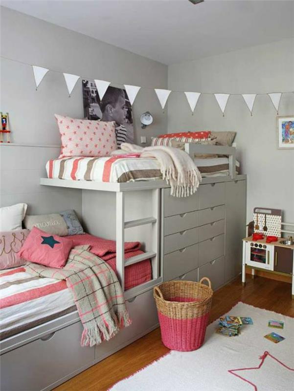 Dekorácia spálne pre dospelých zriadila malú spálňu s dvoma poschodovými posteľami a bielymi trojuholníkovými vlajkami na strope, biely koberec s ružovou hviezdou na podlahe, vankúše a deku v koralových farbách, na stene veľká fotografia dieťaťa