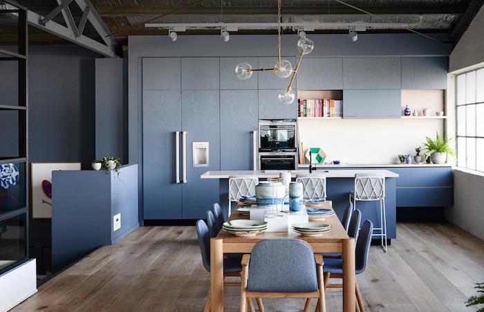 vybavte malú kuchyňu s modrou fasádou a bielym splashbackom, modrý stredový ostrov, jedáleň so stolom z masívneho dreva a drevenými stoličkami s vioeltovým sedadlom