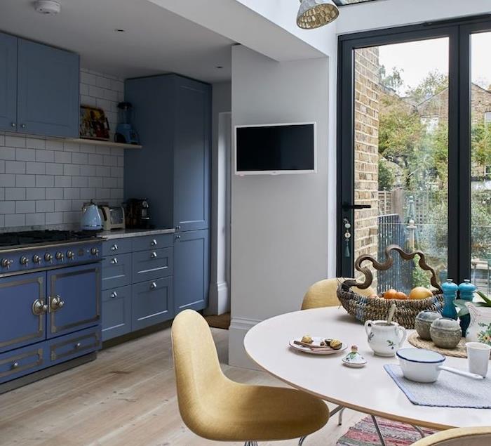 malá modrá kuchyňa s bielou kachľovou linkou, ľahkými parketami, vstupom do jedálne, okrúhly stôl a žlté stoličky