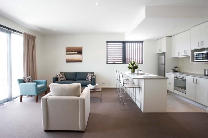inrätta ett litet vitt kök öppet för ett vardagsrum med grå soffa, blå fåtölj och benvit fåtölj, brun matta, separering kök vardagsrum centrala ön