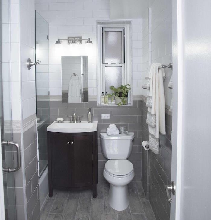 malá biela a sivá kúpeľňa, sivobiele dlaždice a podlaha so sivými parketami, malé zrkadlo, hnedý drevený toaletný stolík