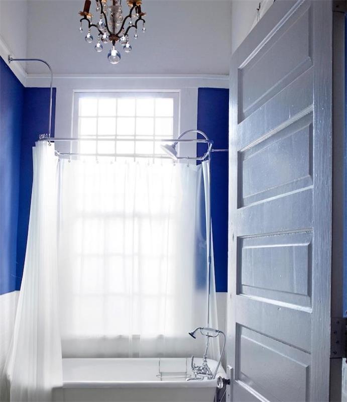 malá luxusná dizajnová kúpeľňa, tmavomodrá stena, biela vaňa a biely sprchový záves, luxusný luster