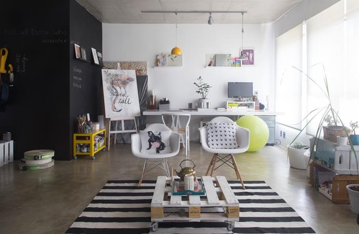 priemyselná podkrovná obývacia izba v čiernej a bielej farbe so zodpovedajúcim paletovým konferenčným stolíkom so škandinávskymi stoličkami a kobercom s lúčom