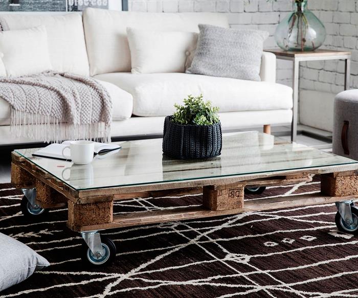 útulná atmosféra v škandinávskej obývačke v bielej farbe s konferenčným stolíkom z paliet a pekným grafickým kobercom v hnedej farbe