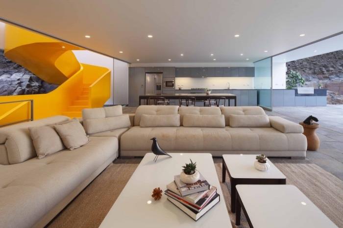 köksidé öppen för vardagsrummet, grå köksfasad, träbord och stolar, betongplattgolv, ljusgrå soffa, vita soffbord, design gul roterande trappa