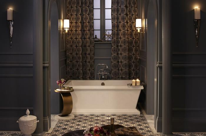 gråvitt badrum, cementplattor, vitt badkar med raka linjer, liten metallpall, grå väggar, tunga gardiner med geometriska mönster