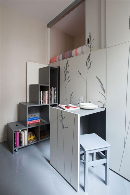 malá malá spálňa pre dospelých v bielej a šedej farbe, úložný priestor po celej výške steny, stenu zdobenú rastlinami nakreslenými sivou farbou
