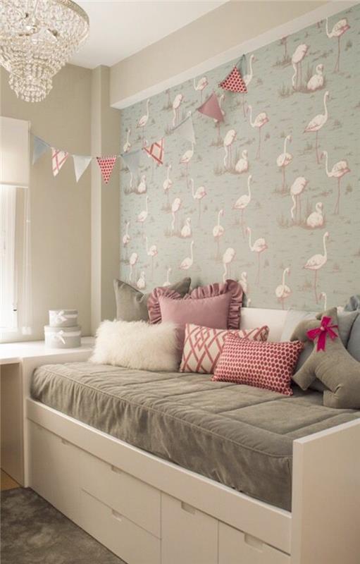 malá výzdoba spálne pre dospelých s ružovými plameniakmi na stene, biela posteľ s veľkými bielymi zásuvkami, sivý matrac do postele a biele, ružové a fuchsiové vankúše, luster s krištáľovými príveskami