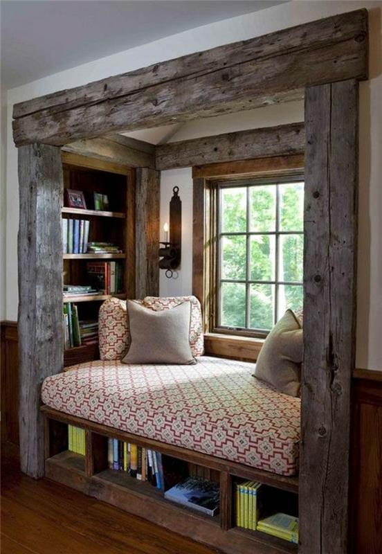 9 m2 spálňa vo výklenku z hrubého svetlošedého dreva s posteľou s červeno -bielym matracom, policami s knihami a nástenným svietnikom z tepaného železa