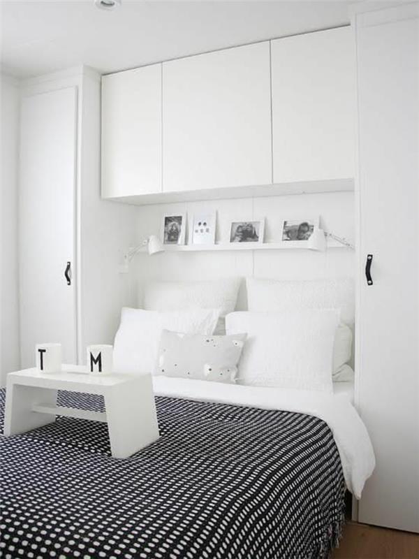 Spálňa 9 m2 s bielym nábytkom a posteľnou prikrývkou z bielych a čiernych dlaždíc, s veľkými bielymi vankúšmi a malým bielym stolom na zdieľanie raňajok do postele