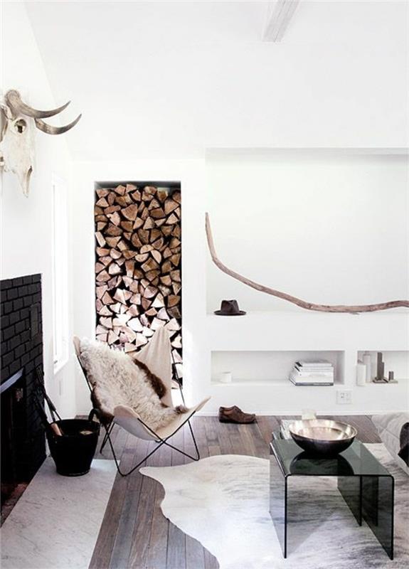 جمجمة حيوان بقرون ، مثبتة على جدار أبيض ، فوق مدفأة سوداء ، داخل غرفة بسيطة على الطراز الشمالي ، حطب وجلود حيوانات