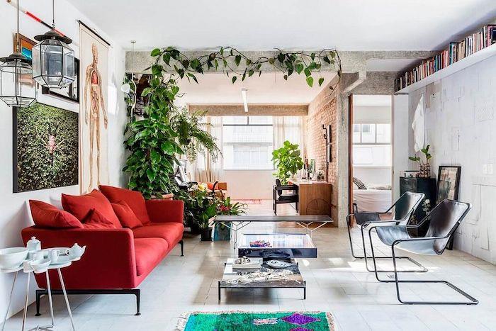 röd soffa och designer svarta stolar arrangerade runt två soffbord i en studio med sittgrupp och skrivbord och sovplats, gröna växter dekoration, lägenhet dekoration