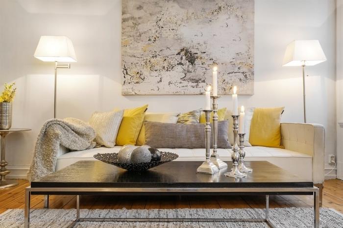 príklad útulnej sivej a žltej obývačky s bielymi stenami a drevenými podlahami s doplnkami, vankúšmi a svietnikmi v sivej farbe