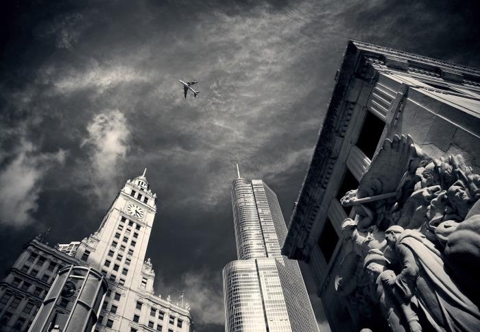 en vacker svartvit bild av ett flygplan som flyger ovanför byggnader, stadsfotografering i svartvitt