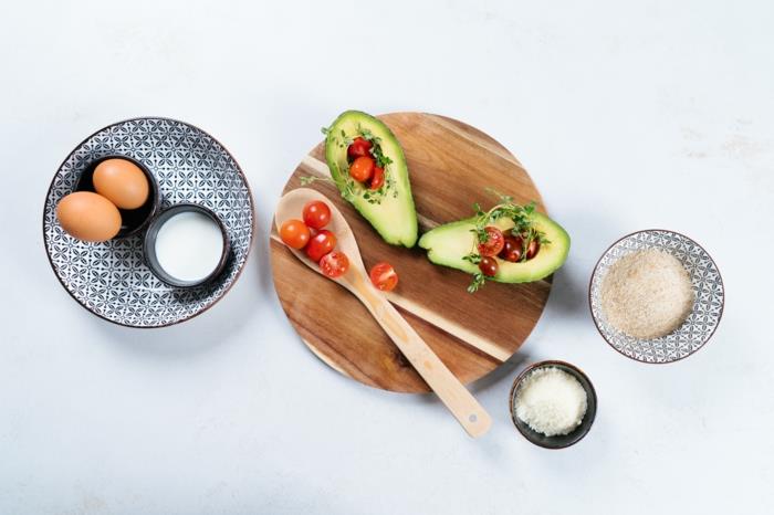 halverade avokado och körsbärstomater, ägg och ströbröd, recept avokado pommes frites, placerat på vit yta