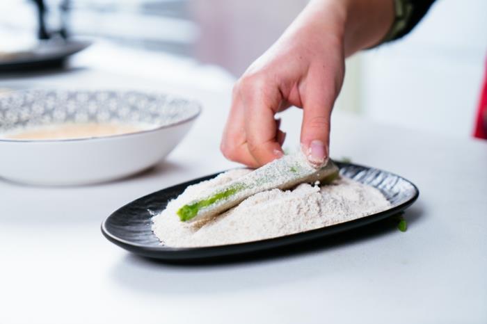 avokado skiva doppad i mjöl, placerad i liten svart tallrik, placerad på vit yta, avokado pommes frites recept
