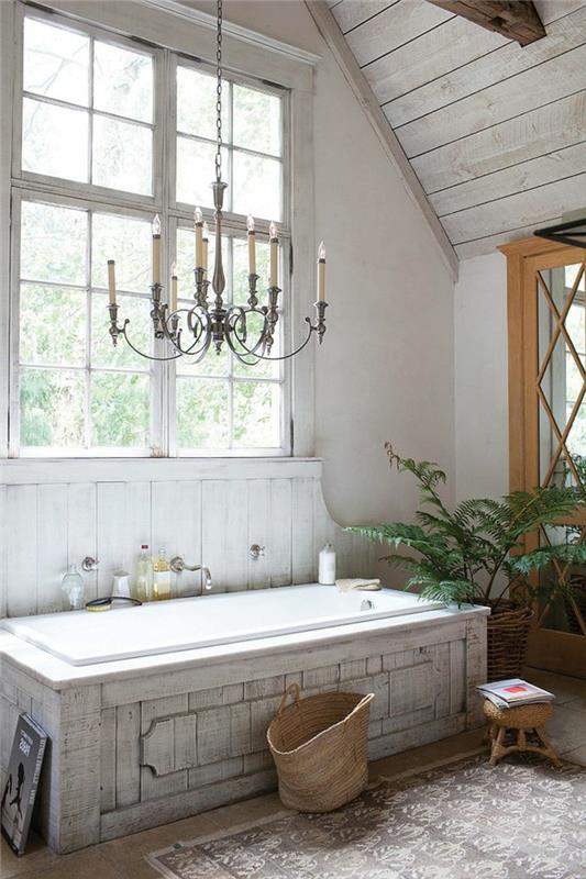rektangulärt vitt badkar, stor vintage ljuskrona, sluttande badrumstak, grön växt
