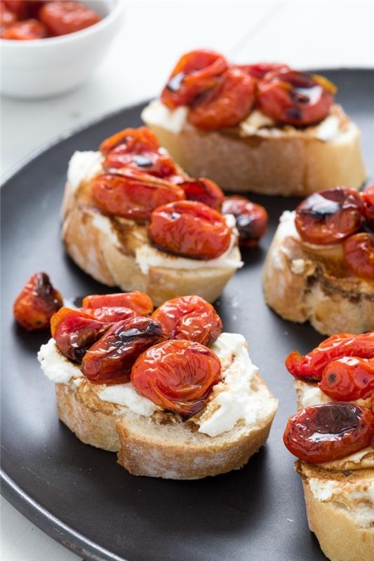 brödskivor, bakade körsbärstomater ovanpå, färskost, veganska hors d'oeuvres, svart tallrik
