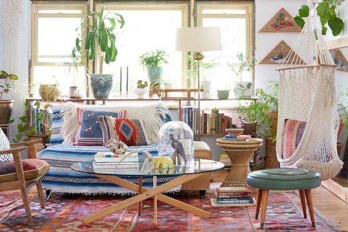 orientálny koberec, hojdačka v interiéri, stôl z dreva a skla, sedačka zdobená farebnými ozdobnými poťahmi a vankúšmi, nízka knižnica, niekoľko izbových zelených rastlín