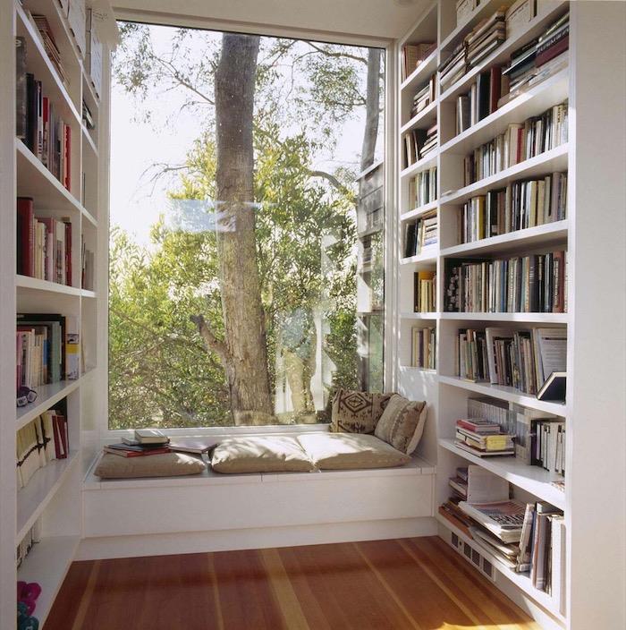 okenná lavica ako kútik na čítanie so sivými vankúšmi na sedenie a bielou knižnicou