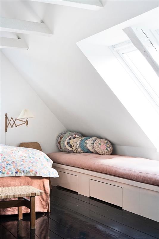 ett sovrum med snett tak med mörkt trägolv och bänk under ett fönster som sitter under sluttningen