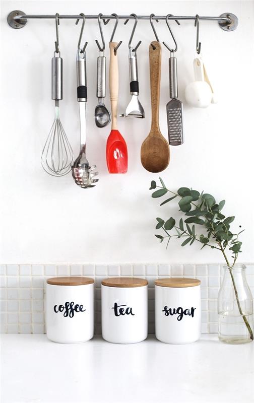 kovová nástenná tyč s háčikmi na zavesenie kuchynského riadu, tri biele nádoby s korkovými viečkami na kávu, čaj a cukor