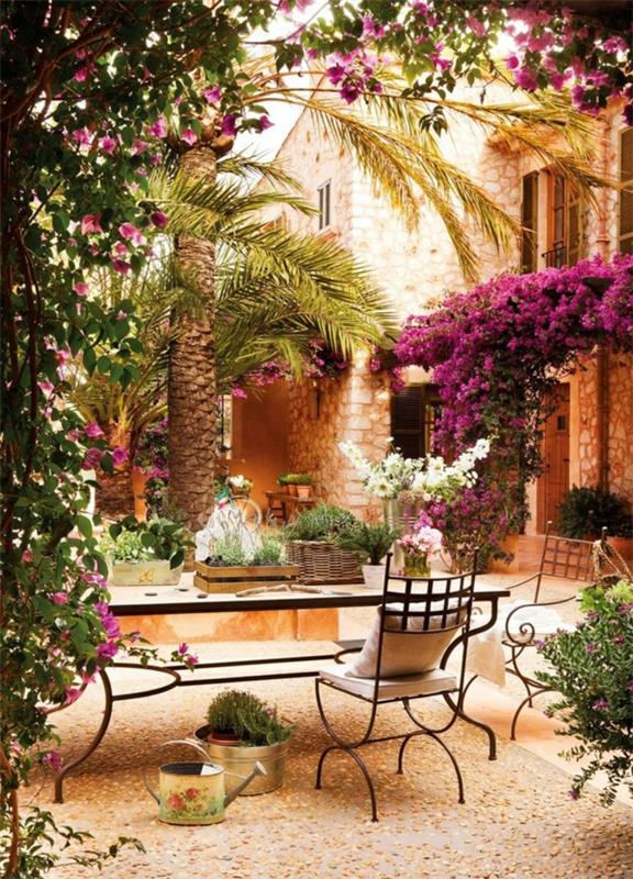 vacker-trädgård-med-dekorativa-småsten-blommor-smidesjärn-stolar