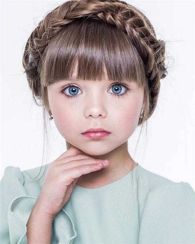 Korunný vrkoč na dlhých vlasoch zostrihaný ofinou, modré oči malé dievčatko a rozkošné modré šaty, detský účes, vrkočový účes, ako upravovať vlasy