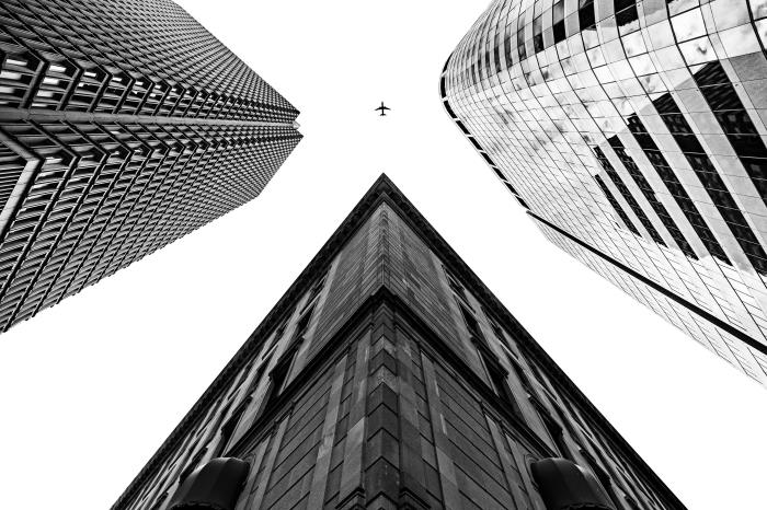 vackert svartvitt foto av ett flygplan på himlen mellan tre höga byggnader, stadsbild med originalperspektiv