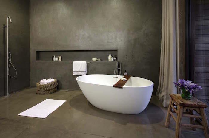 kúpeľňa je celá z voskovaného betónu na drevenej sivej podlahe a stenách s voľne stojacou vaňou a dizajnovou talianskou sprchou