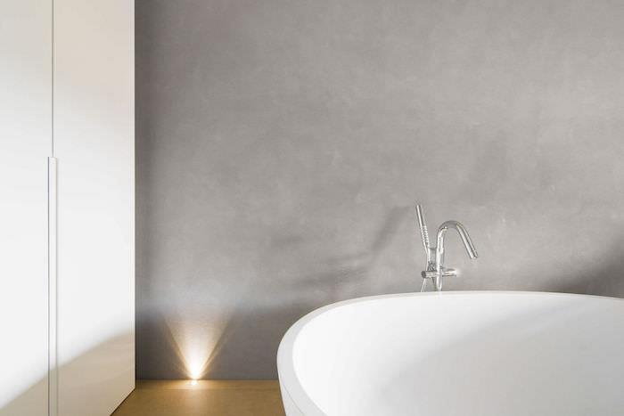 dekoratívny príklad vo stene kúpeľne z voskovaného betónu s voľne stojacou bielou vaňou