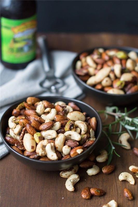 olika typer av nötter, inuti svarta skålar, veganska hors d'oeuvres, träbord