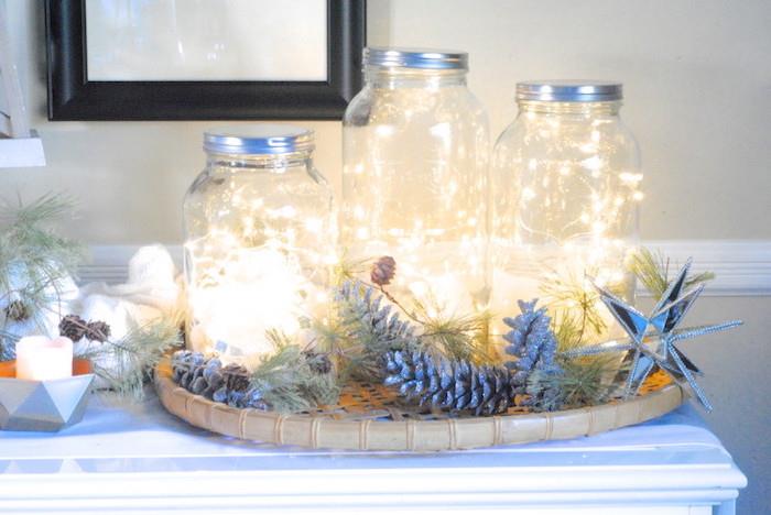 príklad vianočnej dekorácie pre dospelých, sklenená nádoba so svetlou girlandou, dekoratívna kompozícia z konárov a šišok