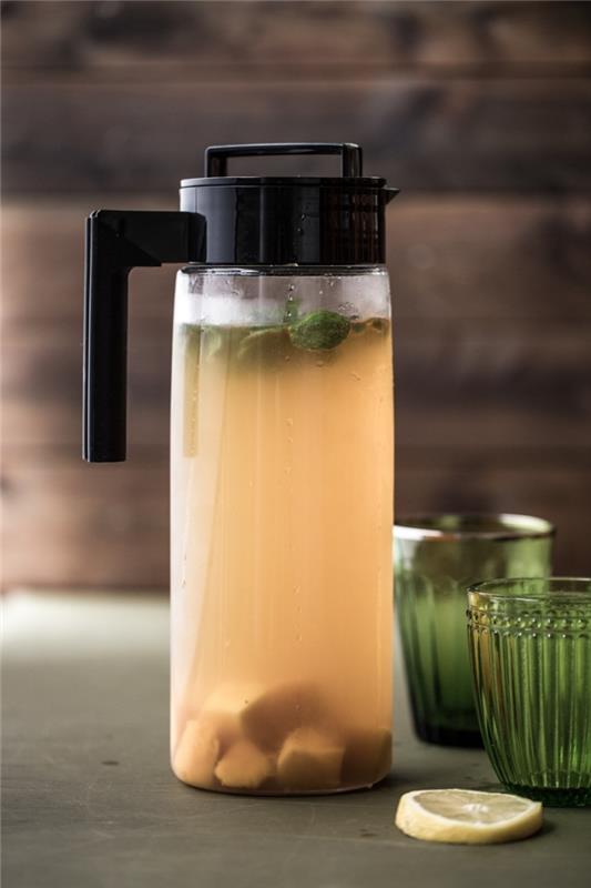 glasflaska fylld med kyldt grönt te med frukt och myntablad, idé kall hälsosam dryck med frukt