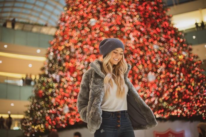 Veselé Vianoce s dievčaťom oblečeným v rifliach a umelom kožuchu v nákupnom centre ozdobenom jedľou obrovskou